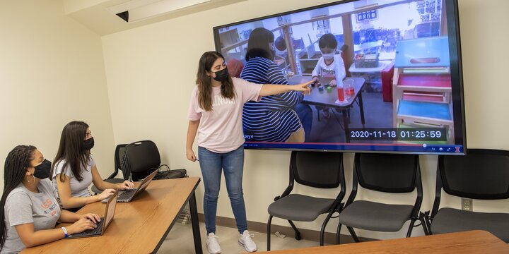 Students observing a child playing on a tv screen