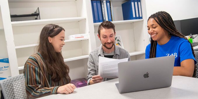 Three students sitting around a computer talking to each other