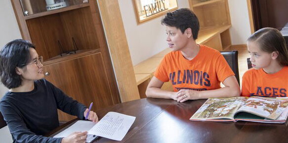 Two students speaking and a child reading a book