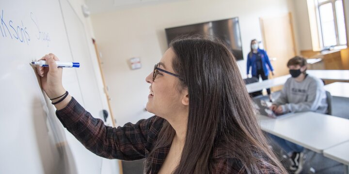 Student writing on a white board with other students in the background
